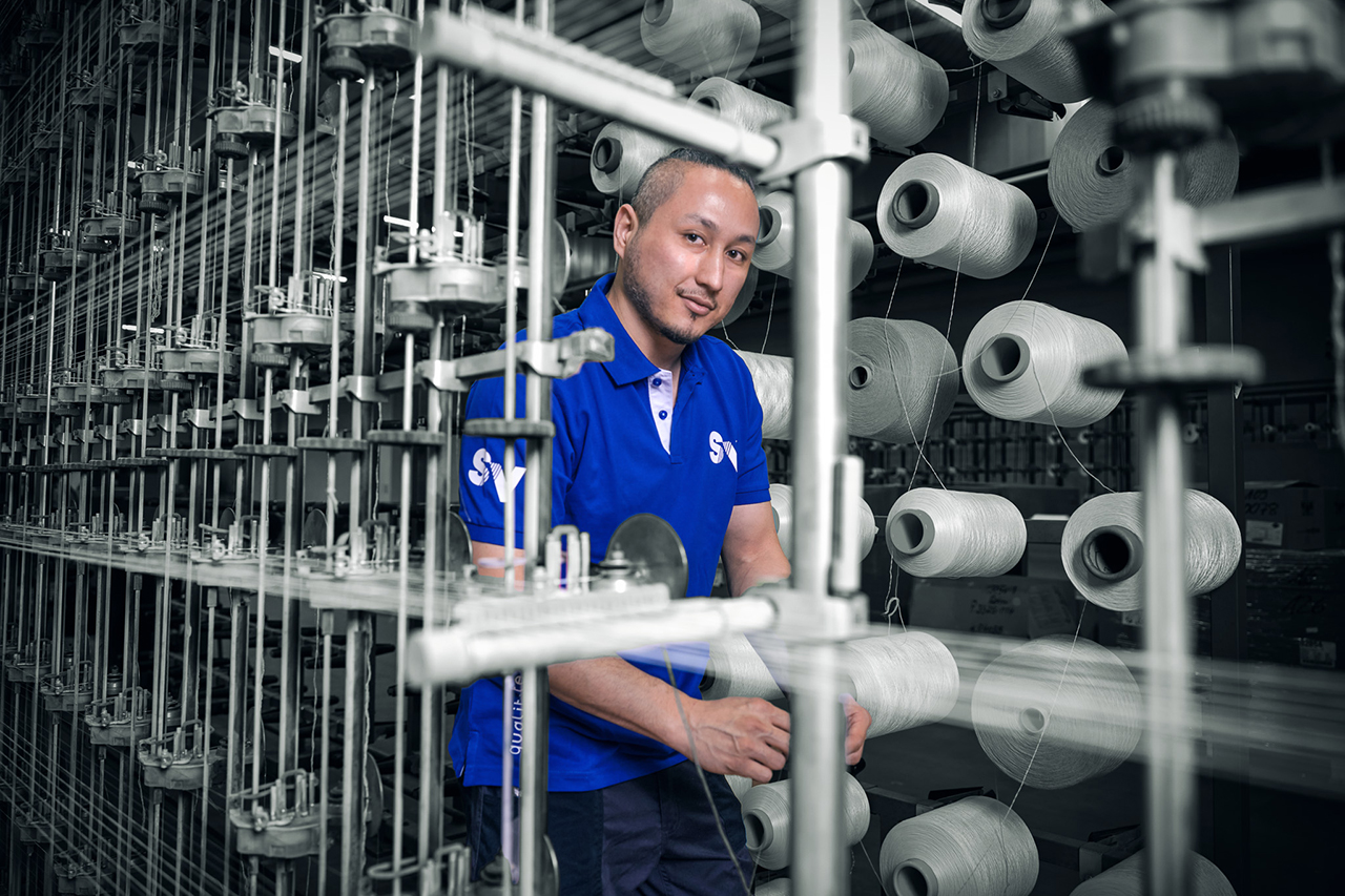 Ein Mann steht in Mitten mehrerer Spulen in der Produktionshalle von Spandauer Velours.